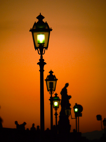 Streetlights and a statue are silouetted against the glow of a setting sun in Florence, Italy.