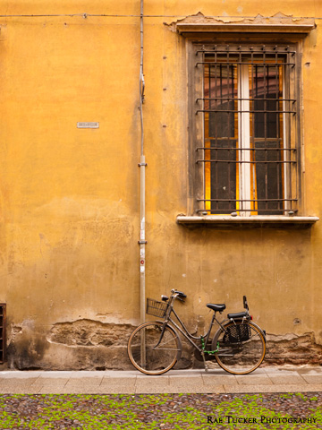 A bicycle leans against a yellow wall in Bologna, Italy