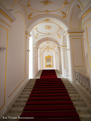 A grand staircase in the Bratislava Castle is draped with a red carpet and sparkles with gold trim