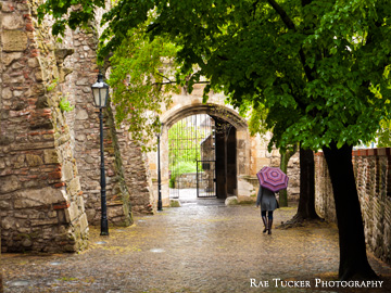A woman carrying a pink umbrella walks down the path leading from the castle.