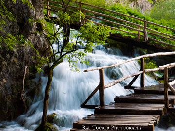 Waterfalls through a forest, surrounding a wooden boardwalk in Plitvice National Park in Croatia