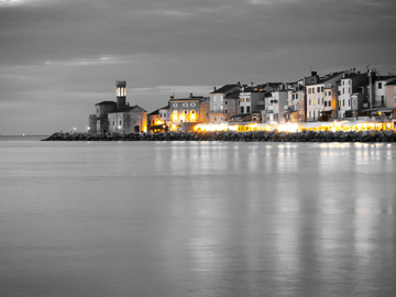 The lights of Piran, Slovenia glow yellow over a black and white image