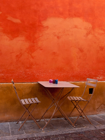 A table and chairs against an orange wall  on a Patio in Parma, Italy