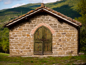 A stone shed with a wooden door stands before the hills of Tuscany, Italy