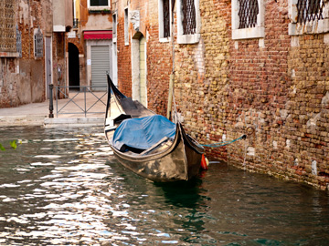 A gondola is tethered to an old, brick building in Venice, Italy