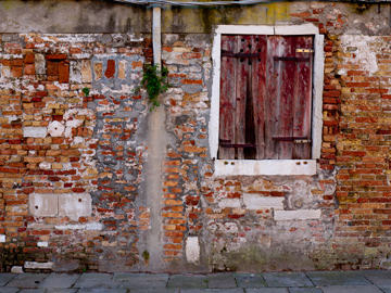 A very worn brick wall and window with red, wooden shutters in Venice, Italy