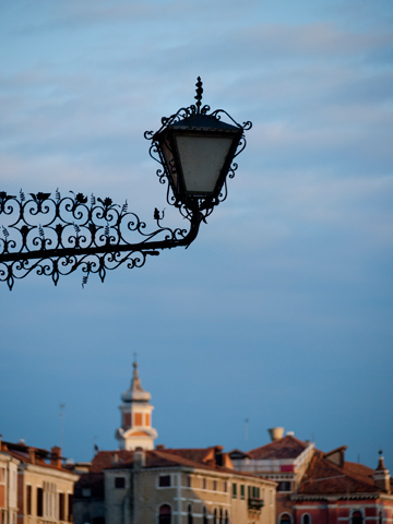 An old-fashioned, intricate street lamp hangs over the city of Venice, Italy