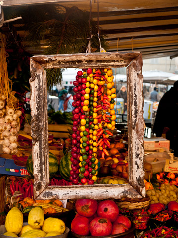 Strings of peppers and a wooden frame hang on display at a market in Rome, Italy