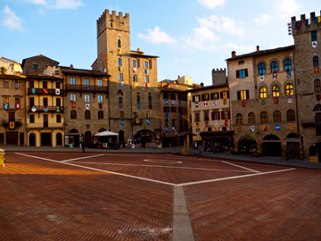 The golden rays of the setting sun wrap themselves over the buildings surrounding Piazza Grande in Arezzo, Italy
